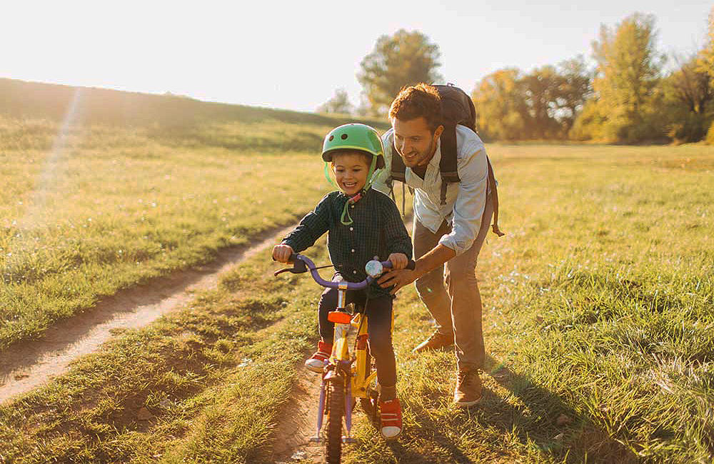 Een papa leert zijn zoontje fietsen op een zonnige dag