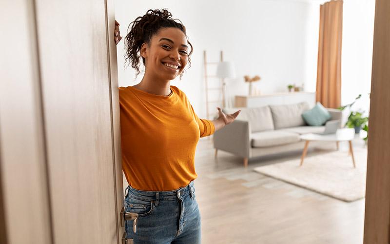 Jonge vrouw opent vriendelijk de deur van haar nieuwe woning