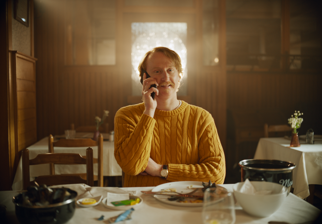 Man van de Crelan-campagnespot belt met zijn smartphone in het restaurant