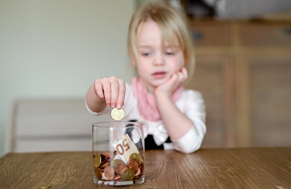 Een jong meisje steekt een spaarcent in haar spaarpot