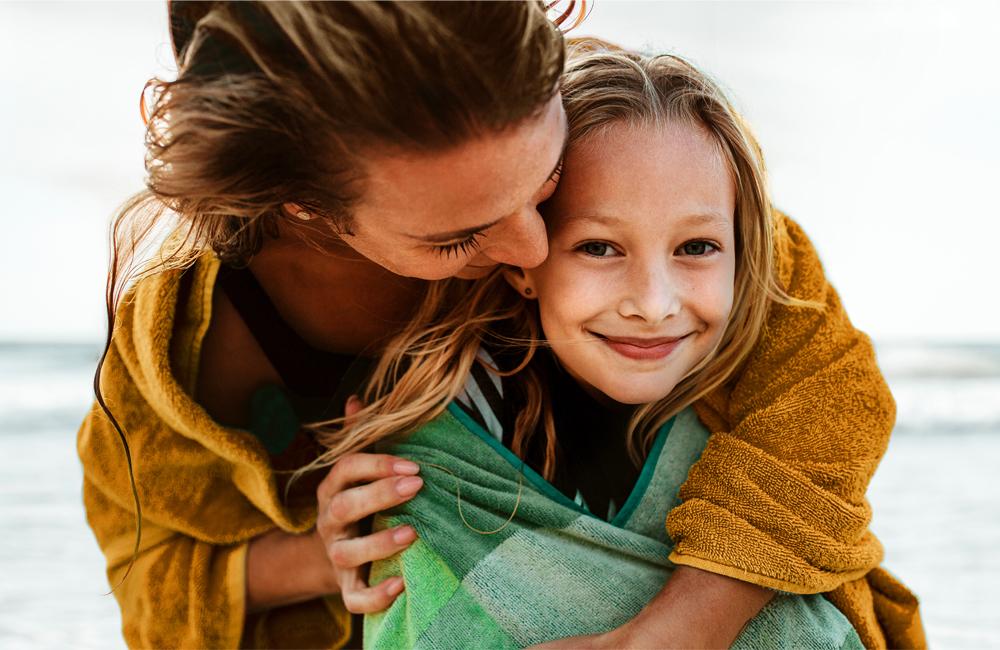 Een jonge vrouw knuffelt haar dochter aan zee