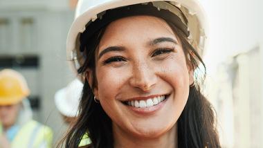 Une jeune femme portant un casque de sécurité sourit sur le chantier