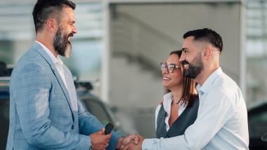 Un couple serre joyeusement la main du vendeur de voitures