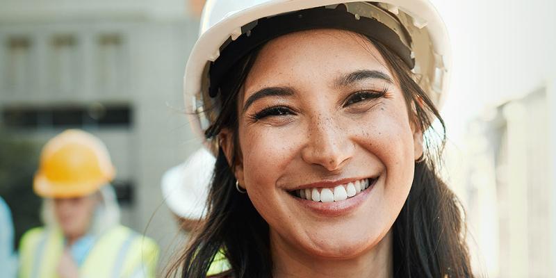 Une jeune femme portant un casque de sécurité sourit sur le chantier