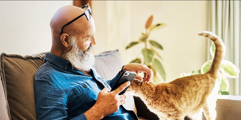 Man met grijze baard en bril streelt zijn kat in de zetel