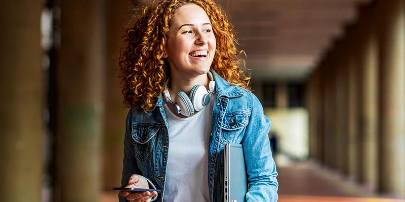Lachende jongedame met hoofdtelefoon en smartphone in de hand