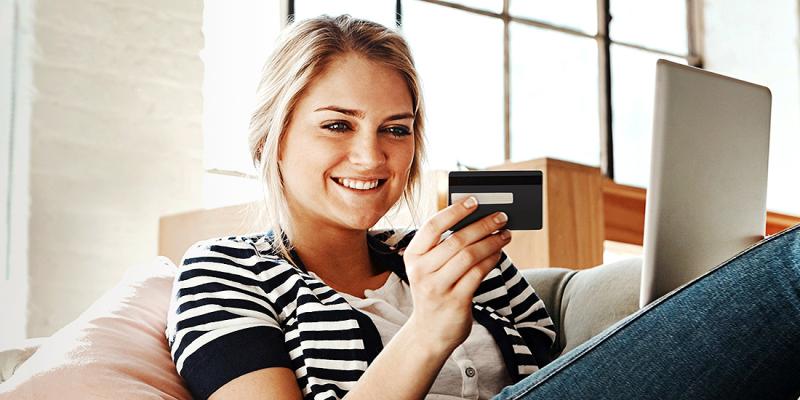 Jeune femme assise dans son fauteuil regarde sa carte bancaire