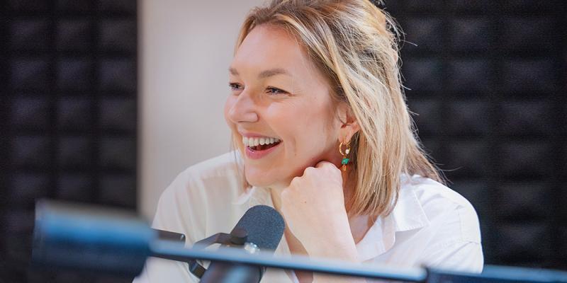 Jonge vrouw met microfoon lachend in de opnamestudio