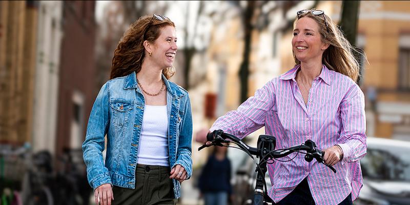Jonge vrouw wandelt met haar fiets aan de hand met een vriendin