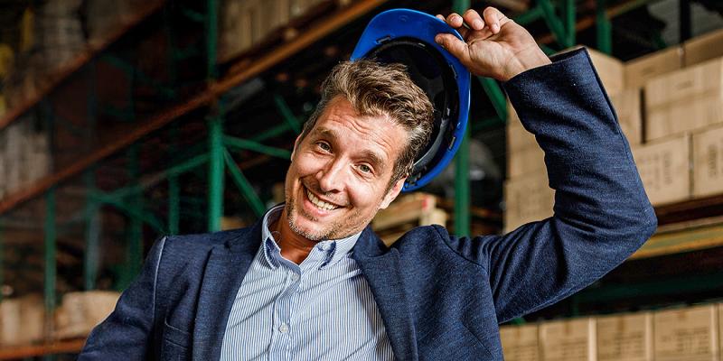 Een jonge zakenman staat vrolijk in zijn magazijn met veiligheidshelm