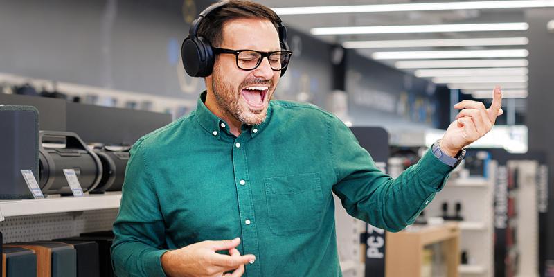 Un homme avec un casque fait semblant de joue de la guitare  avec enthousiasme dans un magasin de musique