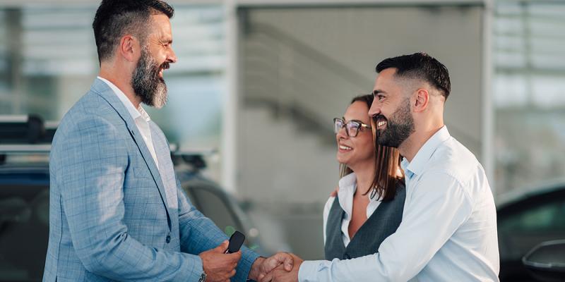 Un couple serre joyeusement la main du vendeur de voitures