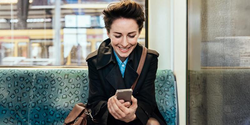 Une femme regarde son smartphone avec un sourire dans le tram