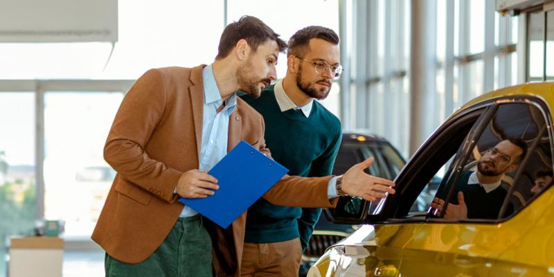 Een jongeman bekijkt een tweedehandswagen met een autoverkoper in de showroom