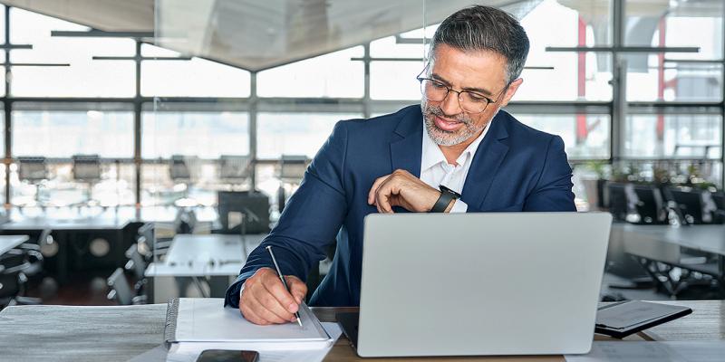 Un homme d'affaires barbu et portant des lunettes prend des notes à son bureau