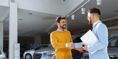 Een man schudt tevreden de hand van zijn autoverkoper in de garage