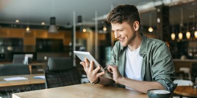 Een jonge ondernemer werkt tevreden op zijn tablet in de koffiehoek