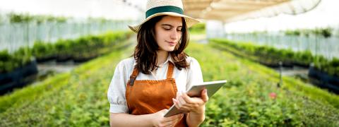 Jonge landbouwster bekijkt een tablet in de serre