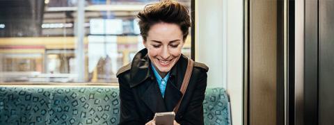 Een vrouw bekijkt lachend haar smartphone op de tram