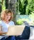 Vrouw bekijkt haar facturen op een laptop in de tuin