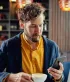 Een man met baard kijkt op zijn smartphone in een koffiebar