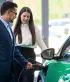 Een jonge vrouw bekijkt een elektrische auto met een verkoper in de showroom