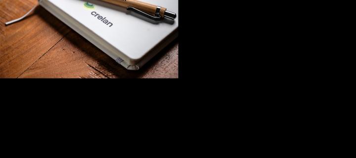 Un agenda et un stylo à bille avec le logo Crelan reposent sur un bureau