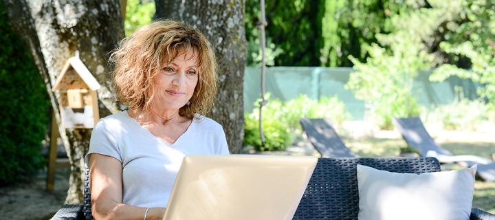 Vrouw bekijkt haar facturen op een laptop in de tuin