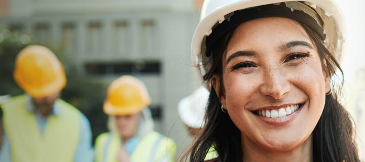 Une jeune femme portant un casque de sécurité sourit sur le chantier
