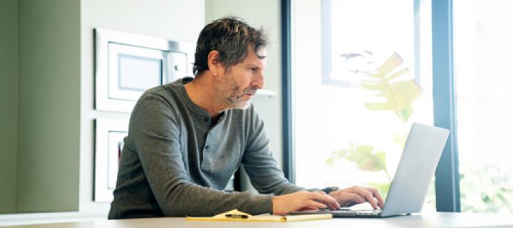 Man bekijkt zijn financiële toestand op zijn laptop aan de keukentafel