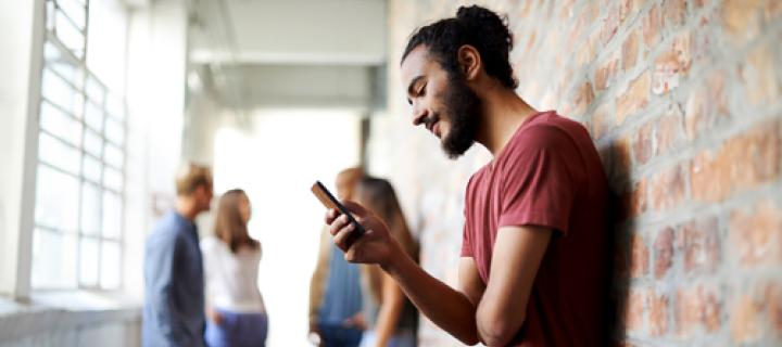 Jonge kerel met dotje kijkt op zijn smartphone in de schoolgang
