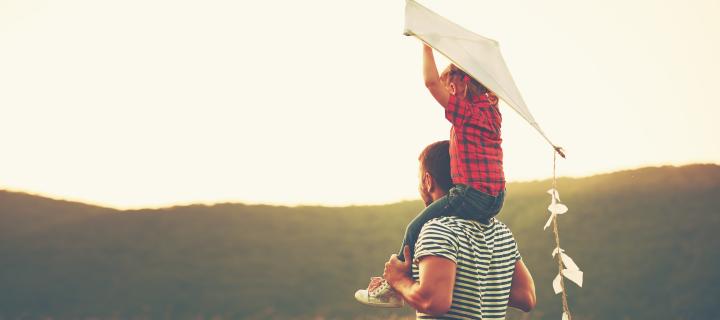 Zoontje met vlieger zit op de schouders van zijn papa