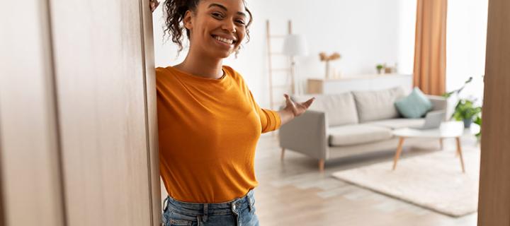 Jonge vrouw opent vriendelijk de deur van haar nieuwe woning