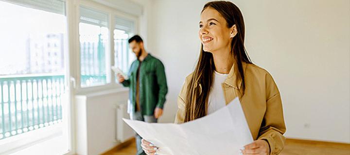 Jonge vrouw lachend in haar nieuwe living met partner op de achtergrond