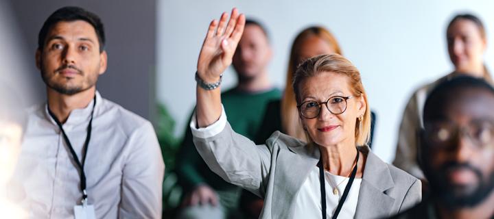 Vrouw in de zaal steekt hand omhoog om een vraag te stellen