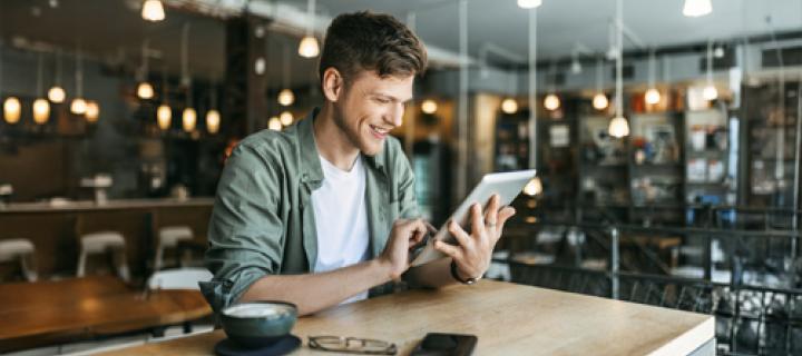 Jongeman kijkt op zijn tablet in een koffiebar