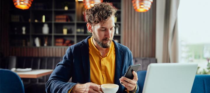 Een man met baard kijkt op zijn smartphone in een koffiebar