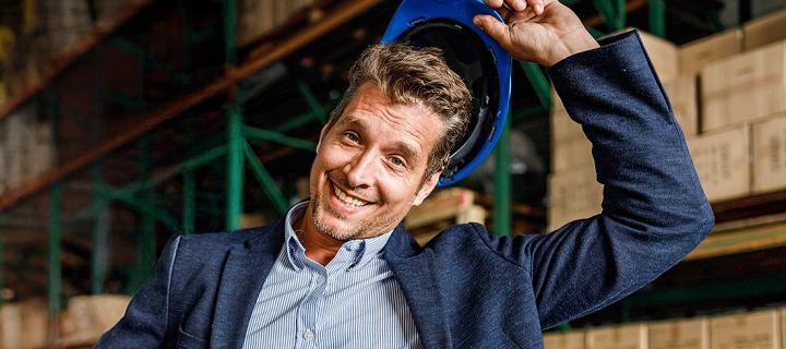 Een jonge zakenman staat vrolijk in zijn magazijn met veiligheidshelm