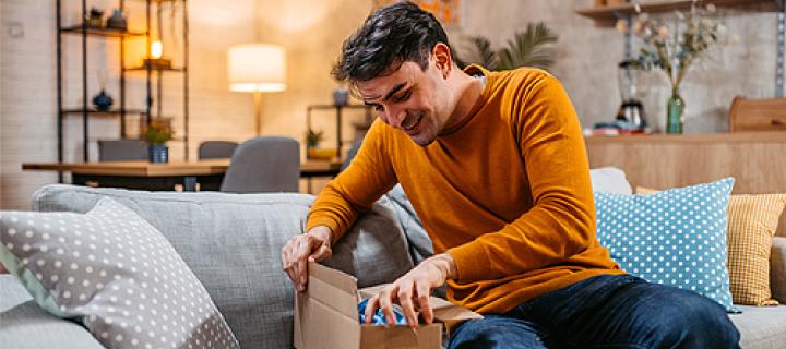 Een man opent tevreden zijn ontvangen pakje in de zetel