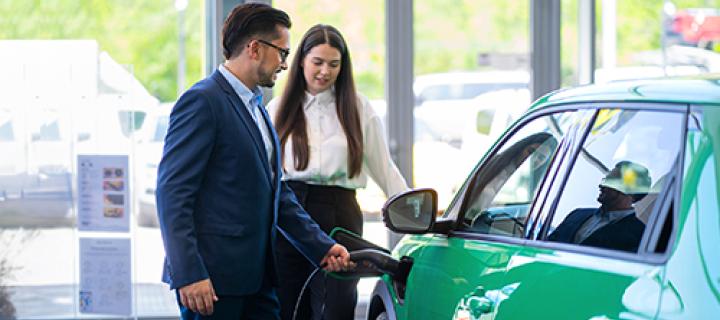Een jonge vrouw bekijkt een elektrische auto met een verkoper in de showroom