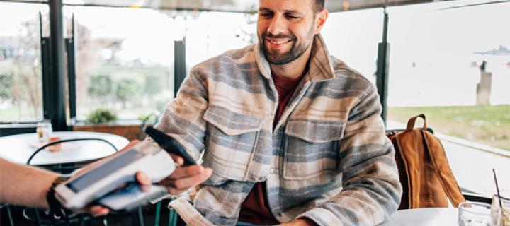 Een tevreden man met baard betaalt contactloos zijn rekening